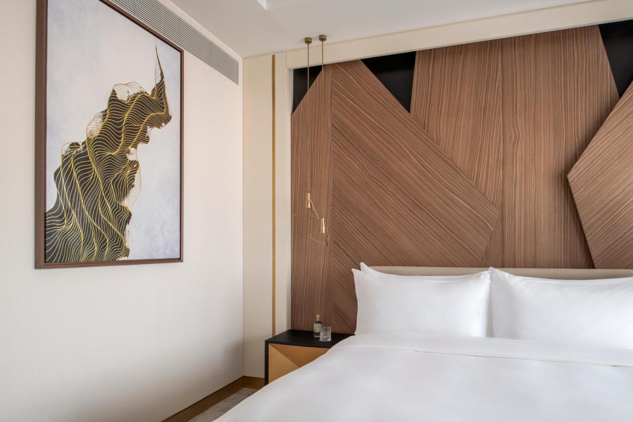 Steigenberger Hotel Doha Exteriör bild The photo shows a modern hotel room with a clean and stylish design. The focal point is a large bed with white linens, set against a wall that features contemporary wooden paneling with geometric shapes. On the left side, there is a piece of artwork 