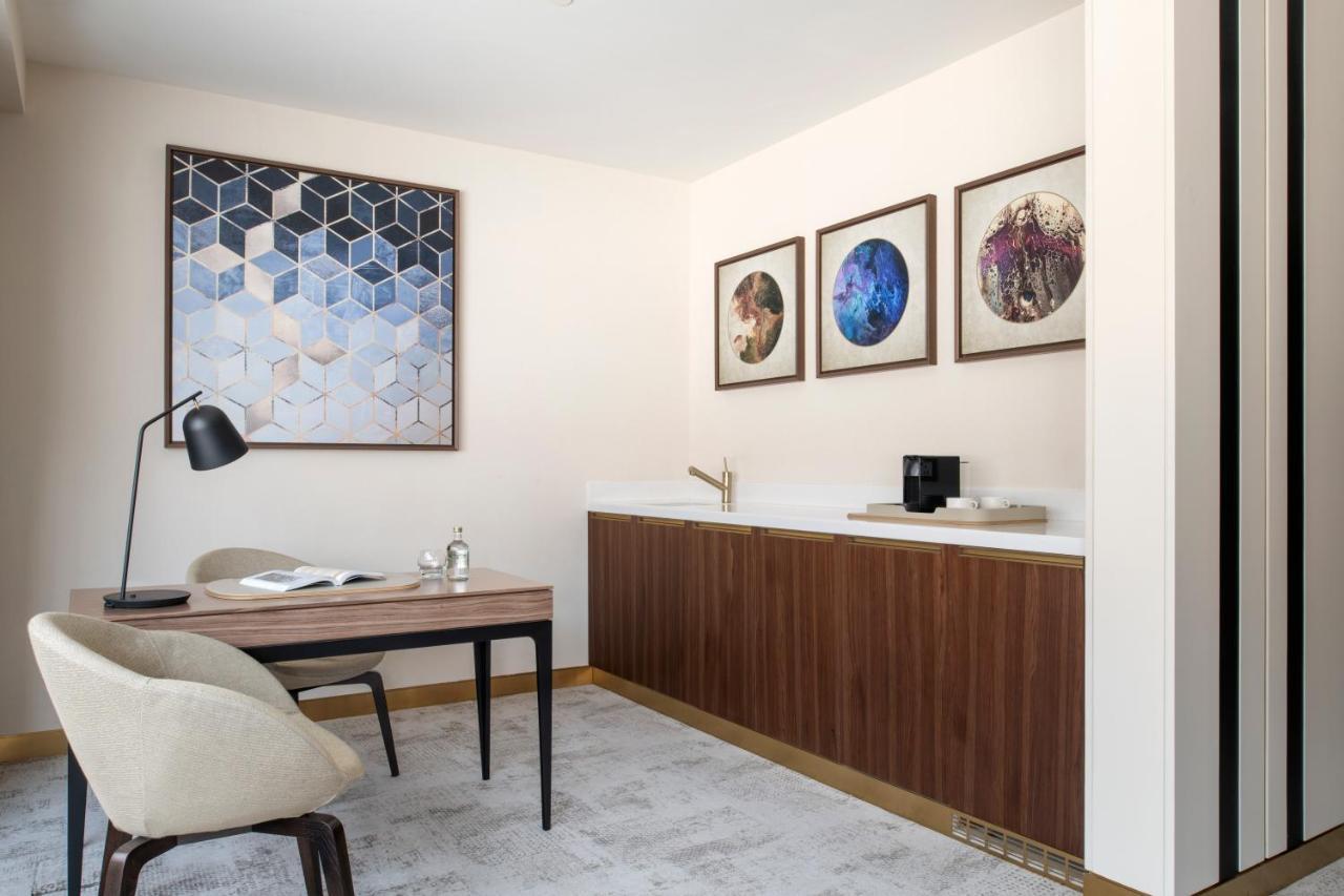 Steigenberger Hotel Doha Exteriör bild The photo shows a modern, stylish office or study area. There's a wooden desk with a minimalist design and a comfortable chair. On the desk, there is an open book and a small decorative item. A sleek desk lamp is positioned on one end of the desk. 

