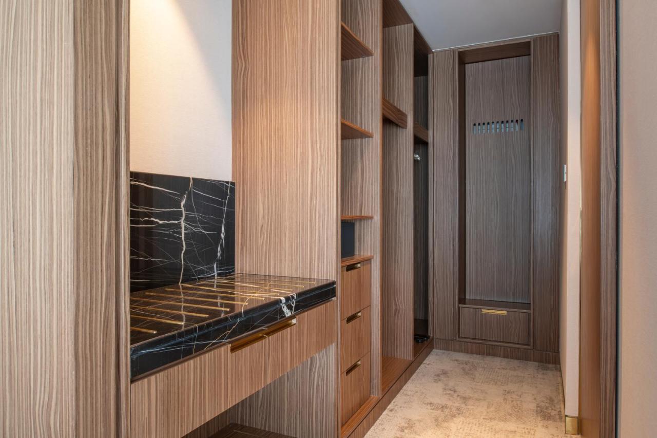 Steigenberger Hotel Doha Exteriör bild The photo shows a well-designed interior space, likely a closet or dressing area. It features wooden cabinetry with a modern finish, including several open shelves for storage. There's a section with a dark marble countertop, which adds an elegant to