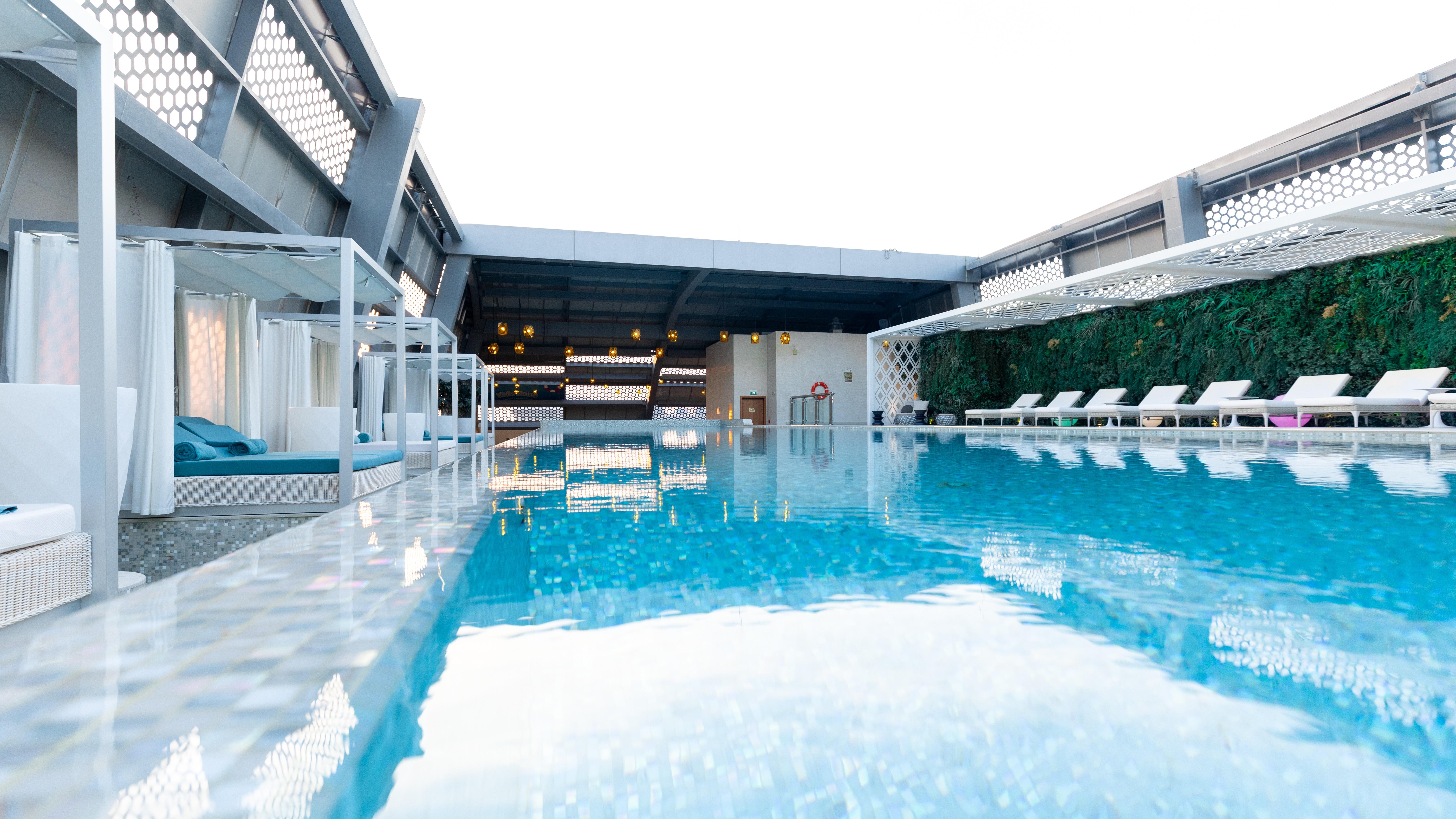 Steigenberger Hotel Doha Exteriör bild The photo shows a modern rooftop swimming pool. The water is clear and reflective, surrounded by white lounge chairs. There are canopies or cabanas along one side, providing shaded seating. The area has a sleek, contemporary design with a mixture of 