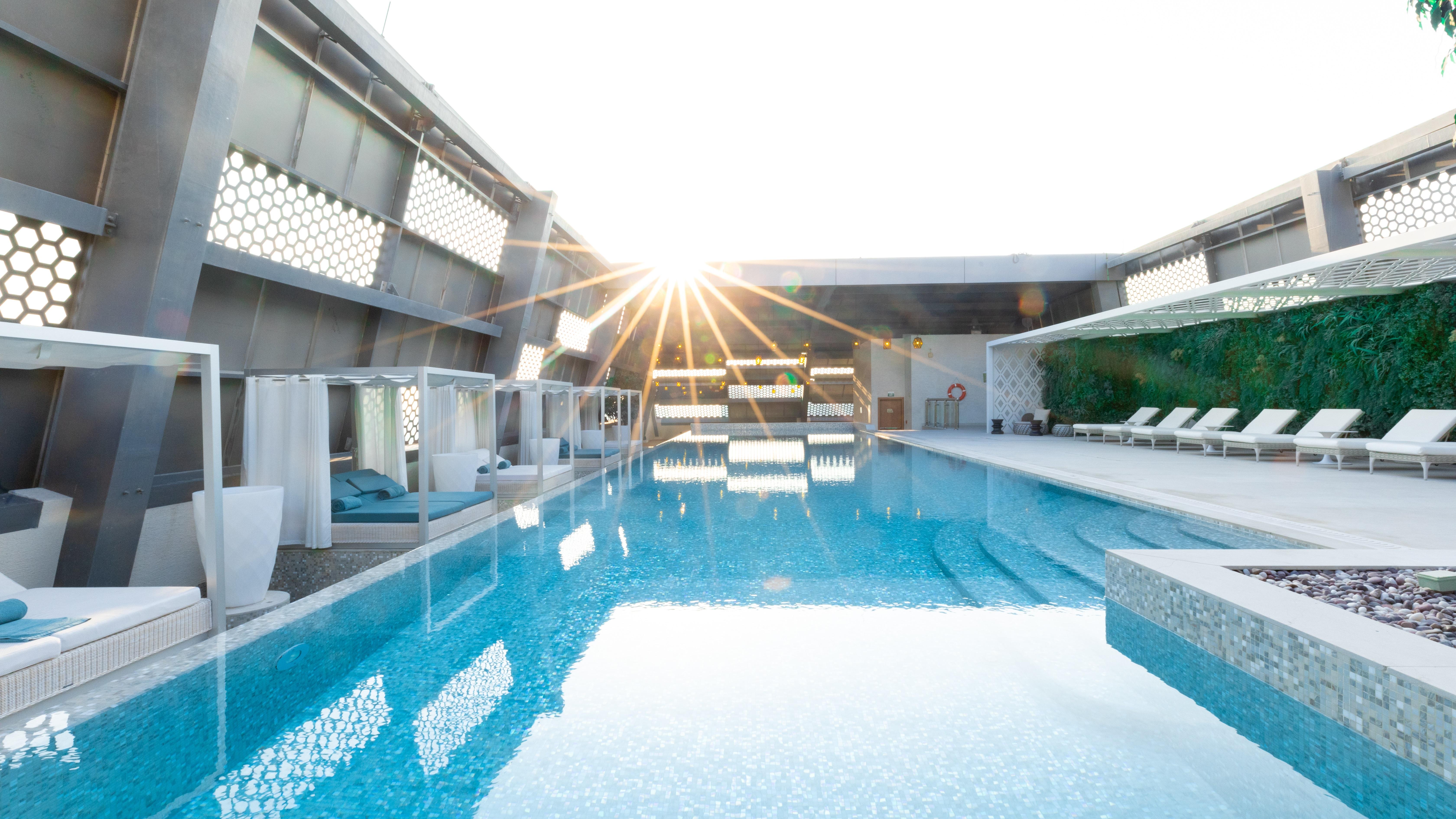 Steigenberger Hotel Doha Exteriör bild The photo shows a modern swimming pool area, likely located on a rooftop, with sunlight shining brightly in the background. The pool features clear, tranquil water that reflects the light and surrounding elements. There are comfortable lounge chairs 