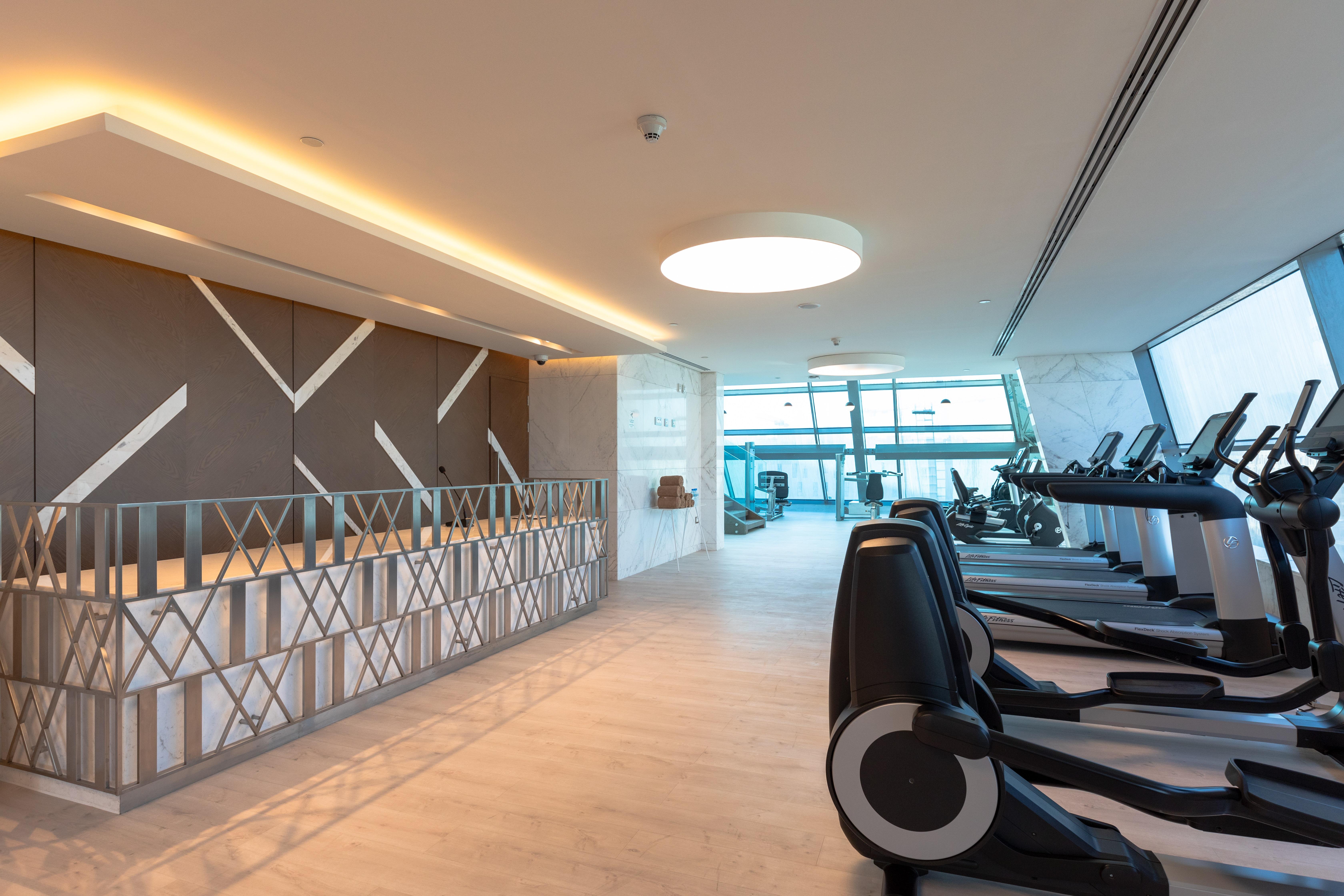 Steigenberger Hotel Doha Exteriör bild The photo shows the interior of a modern gym. On the left side, there is a reception area with a stylish design featuring geometric patterns on the wall. The area is well-lit with natural light coming in from large windows, providing a view outside. 