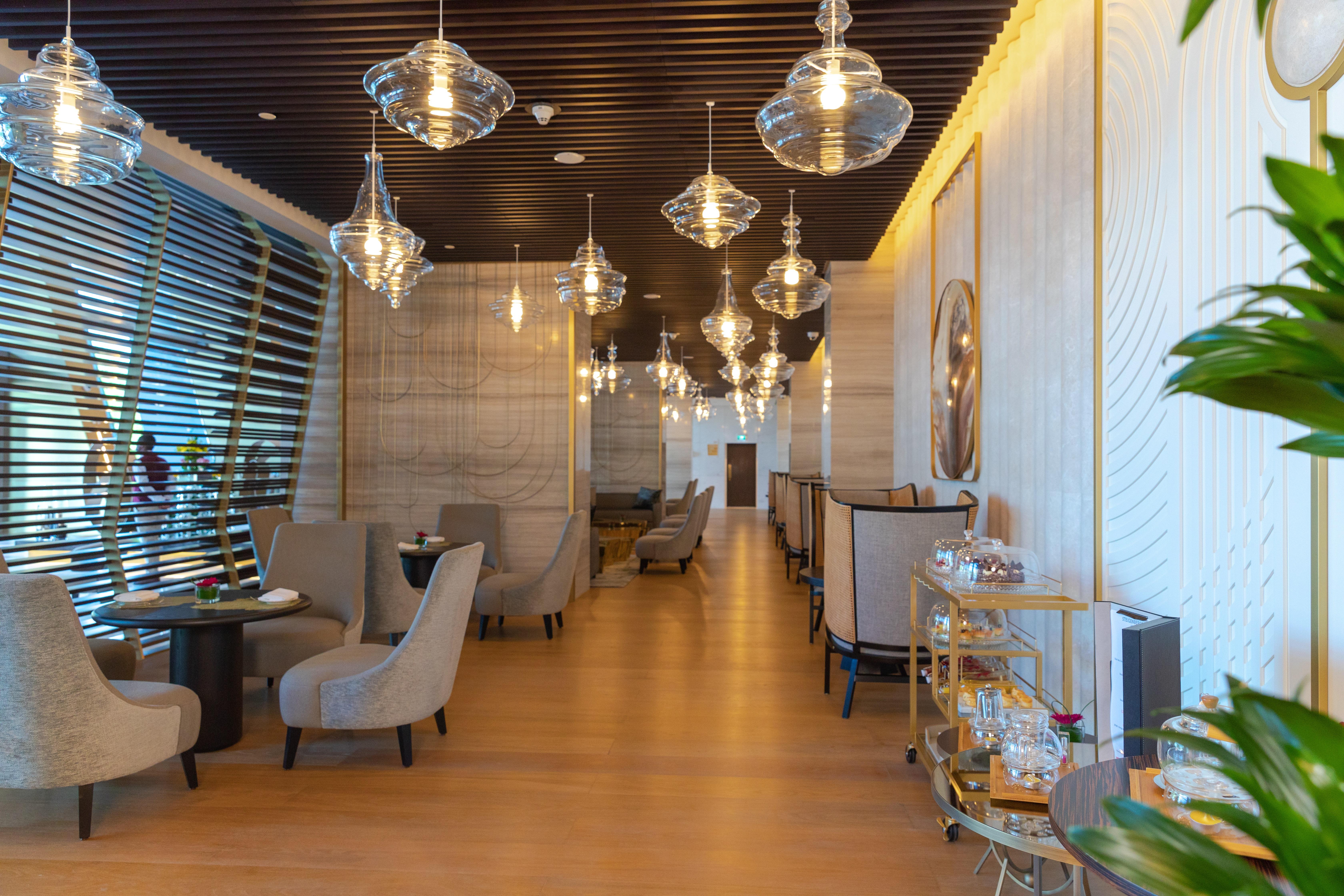 Steigenberger Hotel Doha Exteriör bild The photo shows the interior of a stylish restaurant. It features modern decor with elegant lighting, including several hanging glass pendant lamps. The seating area consists of plush armchairs arranged around small tables, creating an intimate atmos