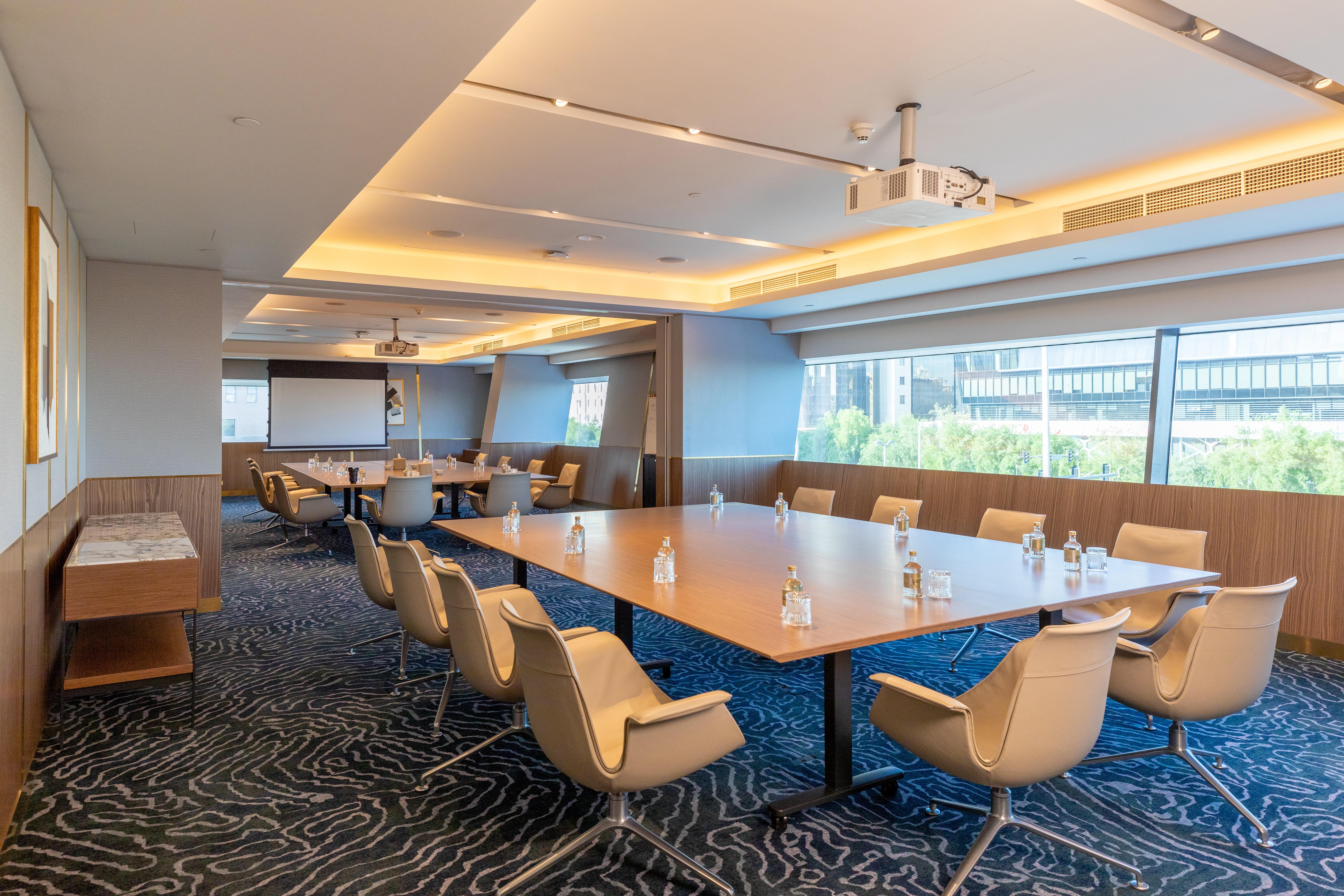 Steigenberger Hotel Doha Exteriör bild The photo shows a modern conference room. It features large windows that let in natural light, illuminating the space. In the center, there is a large rectangular table surrounded by several ergonomic chairs. The table has glass water bottles on it, 