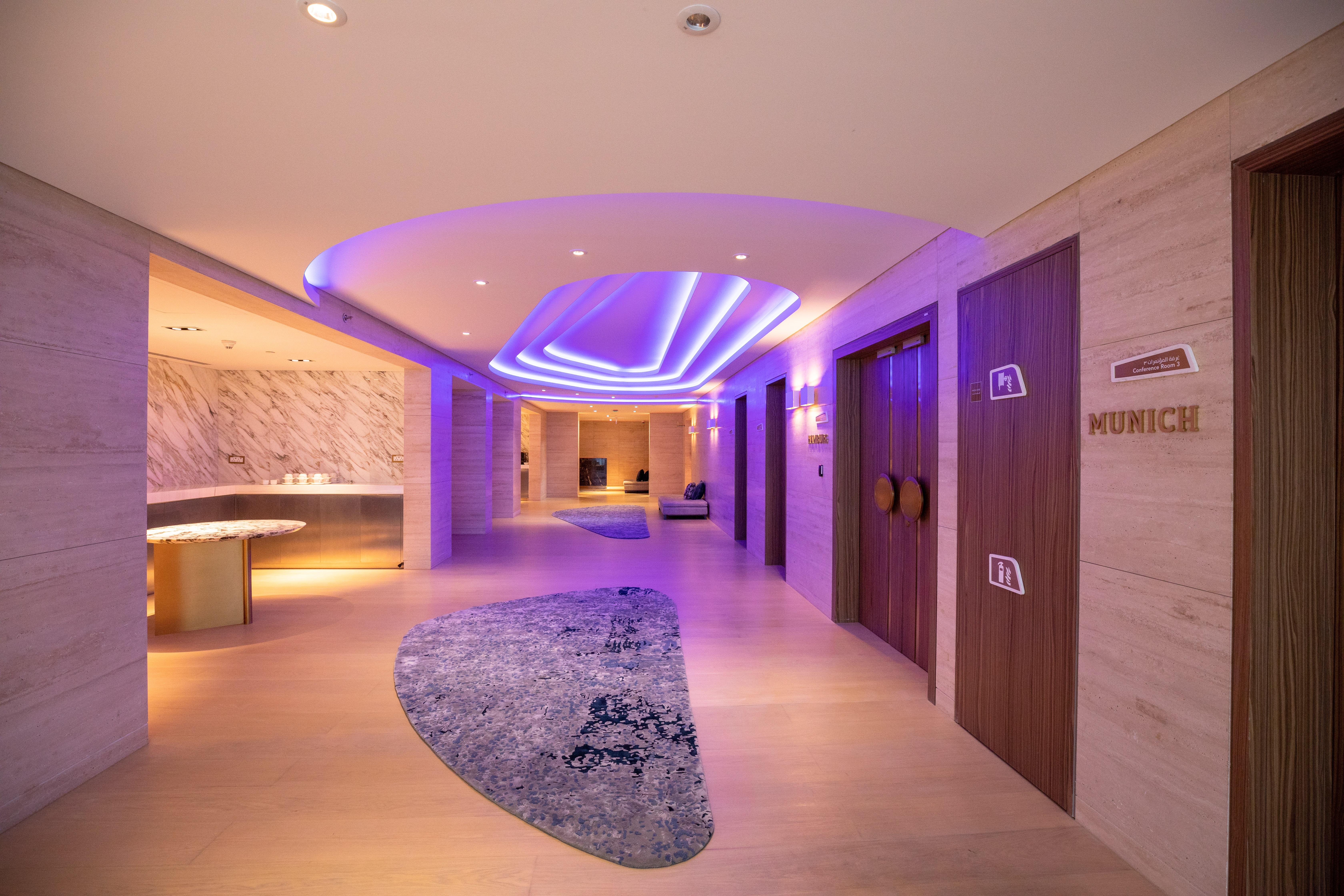 Steigenberger Hotel Doha Exteriör bild The photo shows a modern hallway in a stylish setting. The corridor features soft, ambient lighting with a purple hue, creating a calming atmosphere. On the left side, there is a curved reception area with a smooth surface. The floor is decorated wit