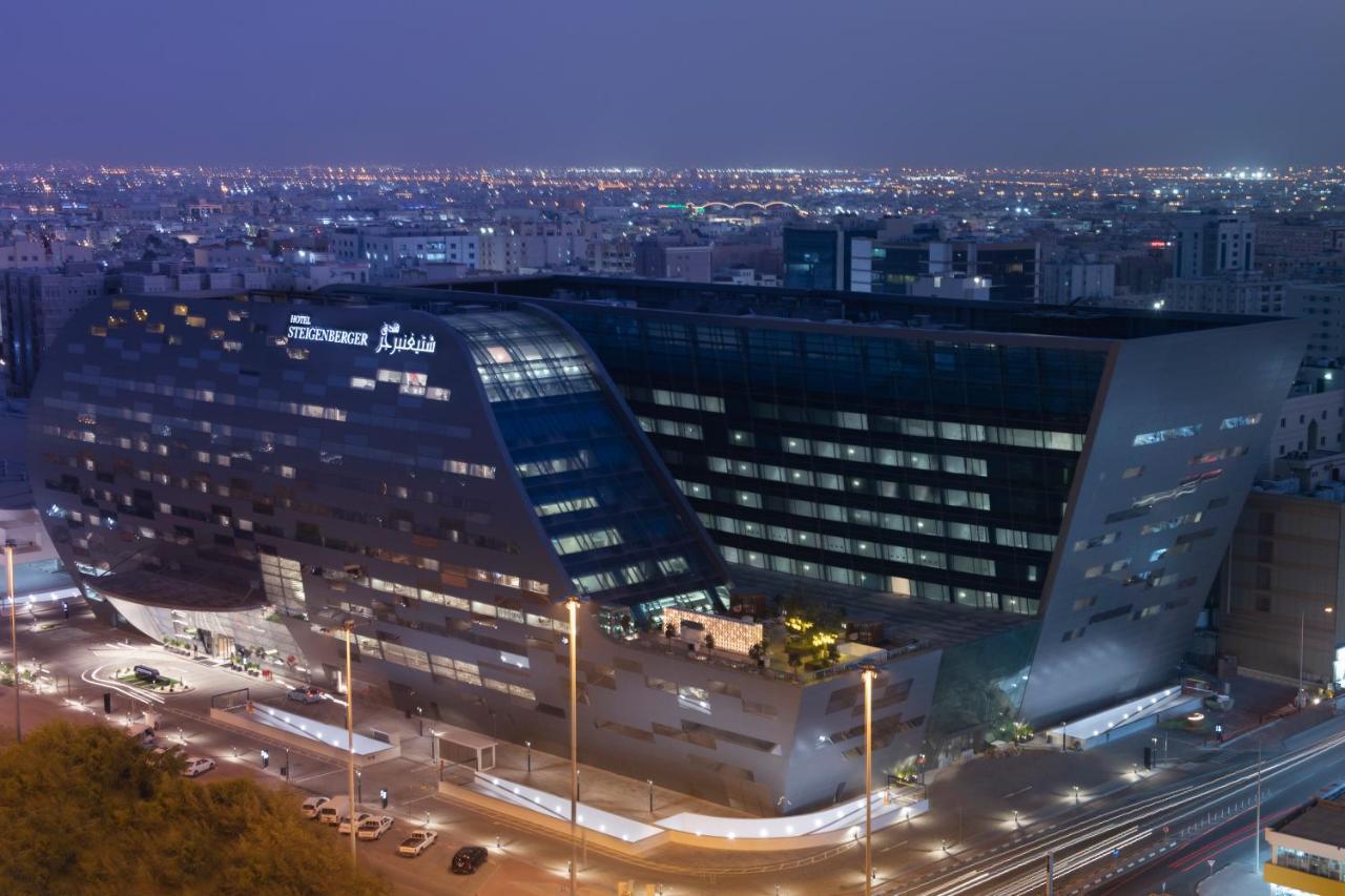 Steigenberger Hotel Doha Exteriör bild The image shows a modern architectural building, likely a hotel or office structure, illuminated at night. The design features a unique angular shape with large glass windows, reflecting the surrounding city lights. The building appears to be part of