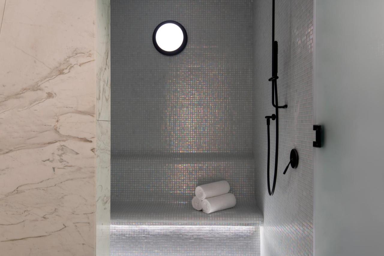Steigenberger Hotel Doha Exteriör bild The photo features a modern shower space. The walls are adorned with small mosaic tiles that create a sleek and reflective surface. There is a round window that allows natural light to enter, enhancing the ambiance. A black shower head and faucet are