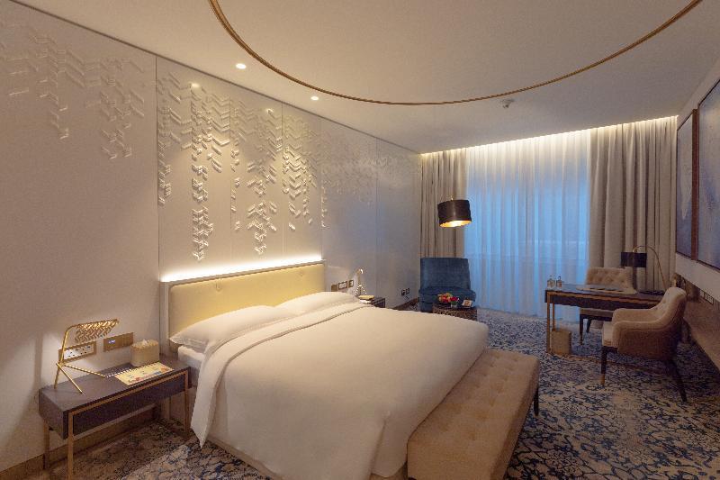 Steigenberger Hotel Doha Exteriör bild The photo shows a modern hotel room featuring a contemporary design. The room includes a large bed with a padded headboard, positioned against a textured wall with decorative patterns. To the side, there is a stylish bedside table with a lamp. A comf