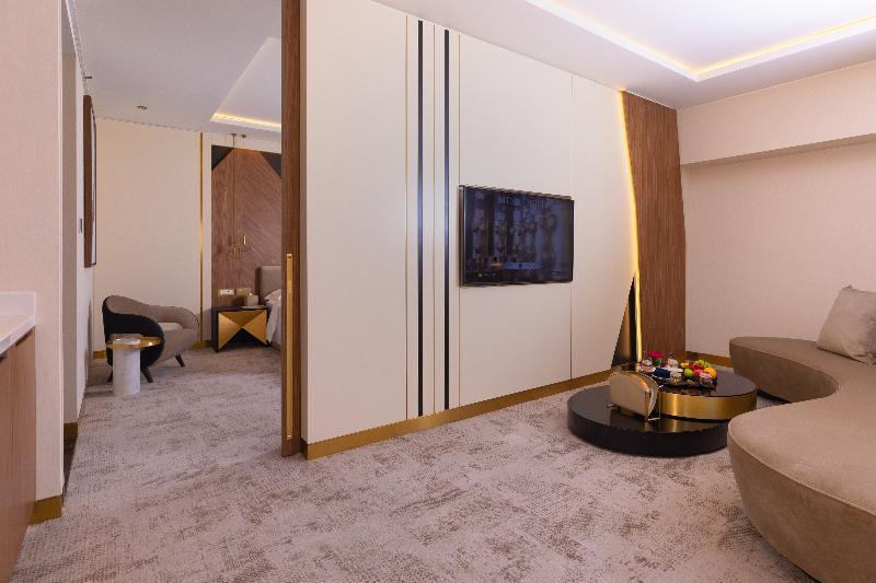 Steigenberger Hotel Doha Exteriör bild The photo shows a modern and stylish hotel room or lounge area. The space features a light-colored carpet and walls, with a sleek design. There's a flat-screen TV mounted against a white wall, which has accents of wood and gold. In the foreground, th