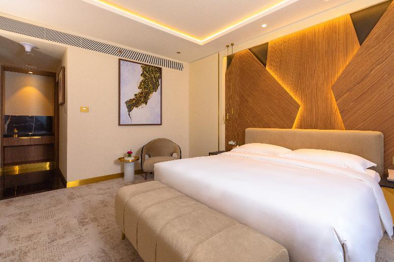 Steigenberger Hotel Doha Exteriör bild The photo shows a modern hotel room featuring a comfortable bed with a plush white duvet, flanked by elegant decorative elements. The headboard has a stylish wood grain design, accompanied by warm lighting that creates a cozy atmosphere. A small seat