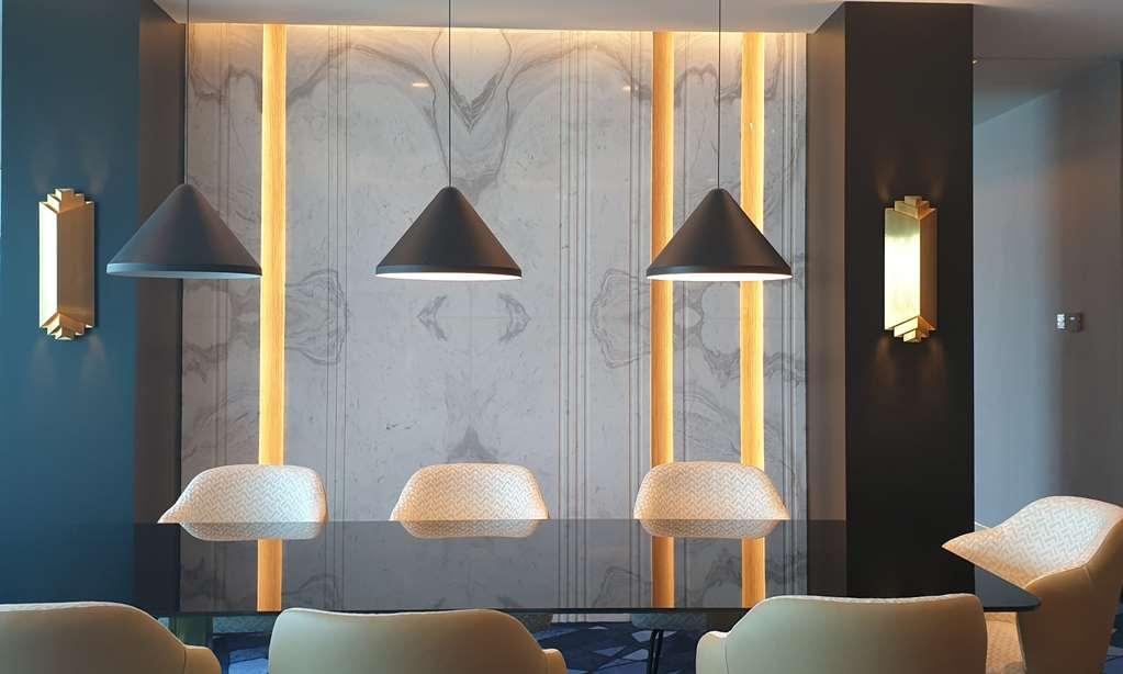Steigenberger Hotel Doha Rum bild The photo showcases a modern interior space featuring a sleek design. The focal point is a wall adorned with a marble-like texture, enhanced by vertical lighting strips that add warmth to the environment. Above a table or counter are three pendant li