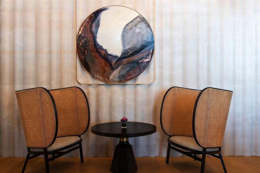Steigenberger Hotel Doha Restaurang bild The photo showcases a stylish and modern seating area featuring two elegantly designed chairs with curved, woven backs and light-colored cushions. Between the chairs is a small round table with a black base. Above the table hangs a large circular art